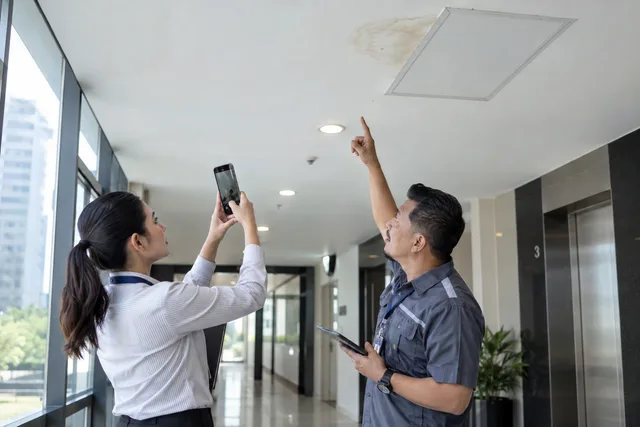 A facilities team photographs a ceiling stain during an inspection.