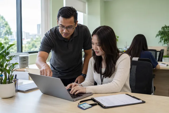 An IT technician helps a new employee test their prepared laptop.