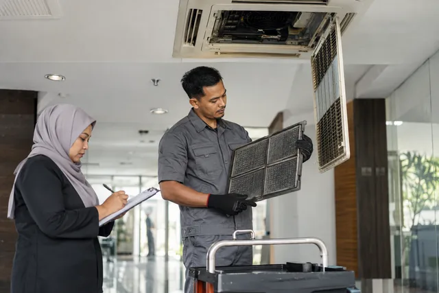 A technician checks an air-conditioning filter while a supervisor records the service.